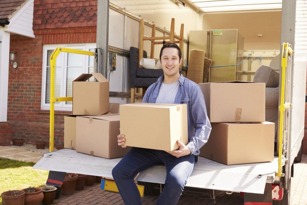 Man sitting on a Luton van tail lift unloading boxes